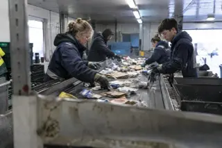 Dans la cabine d’un centre de tri des déchets recyclables, quatre trieurs retirent des emballages d’un tapis roulant