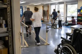 Séance de rééducation dans un centre de soins de suite : un kinésithérapeute guide un patient entre des barres parallèles