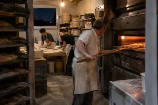 Boulangers au travail à quatre heures du matin dans le fournil, l’un enfourne des baguettes à la pelle