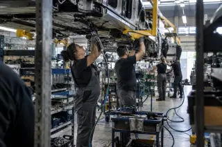 Opératrices et opérateurs sur une ligne d’assemblage automobile, bras levés sous une caisse portée par le convoyeur